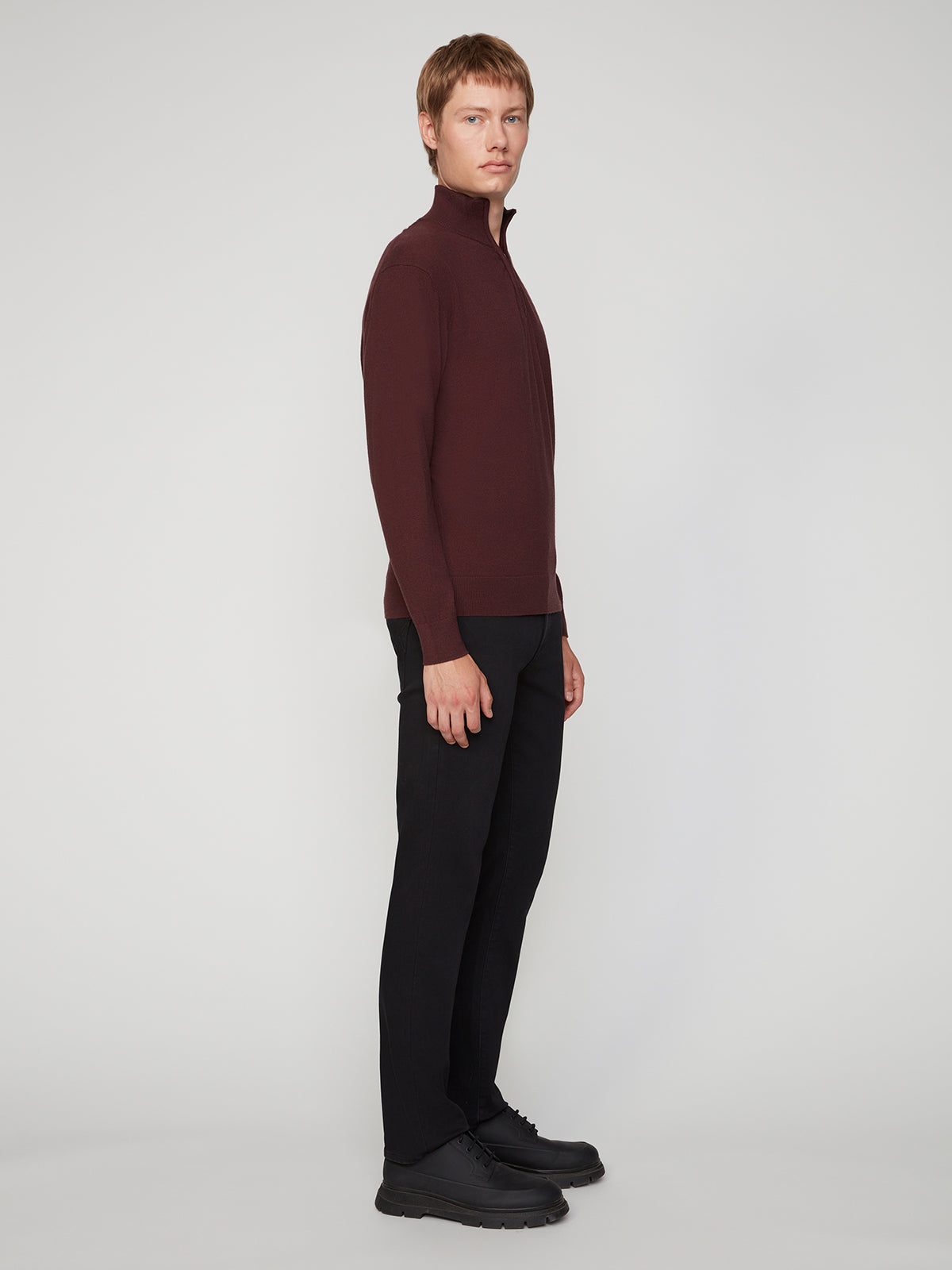 A man stands sideways against a plain gray background, wearing a maroon zip-up sweater, black shoes, and PROJEK RAW MENS BARU STRAIGHT FIT COLORED DENIM JEAN in black.