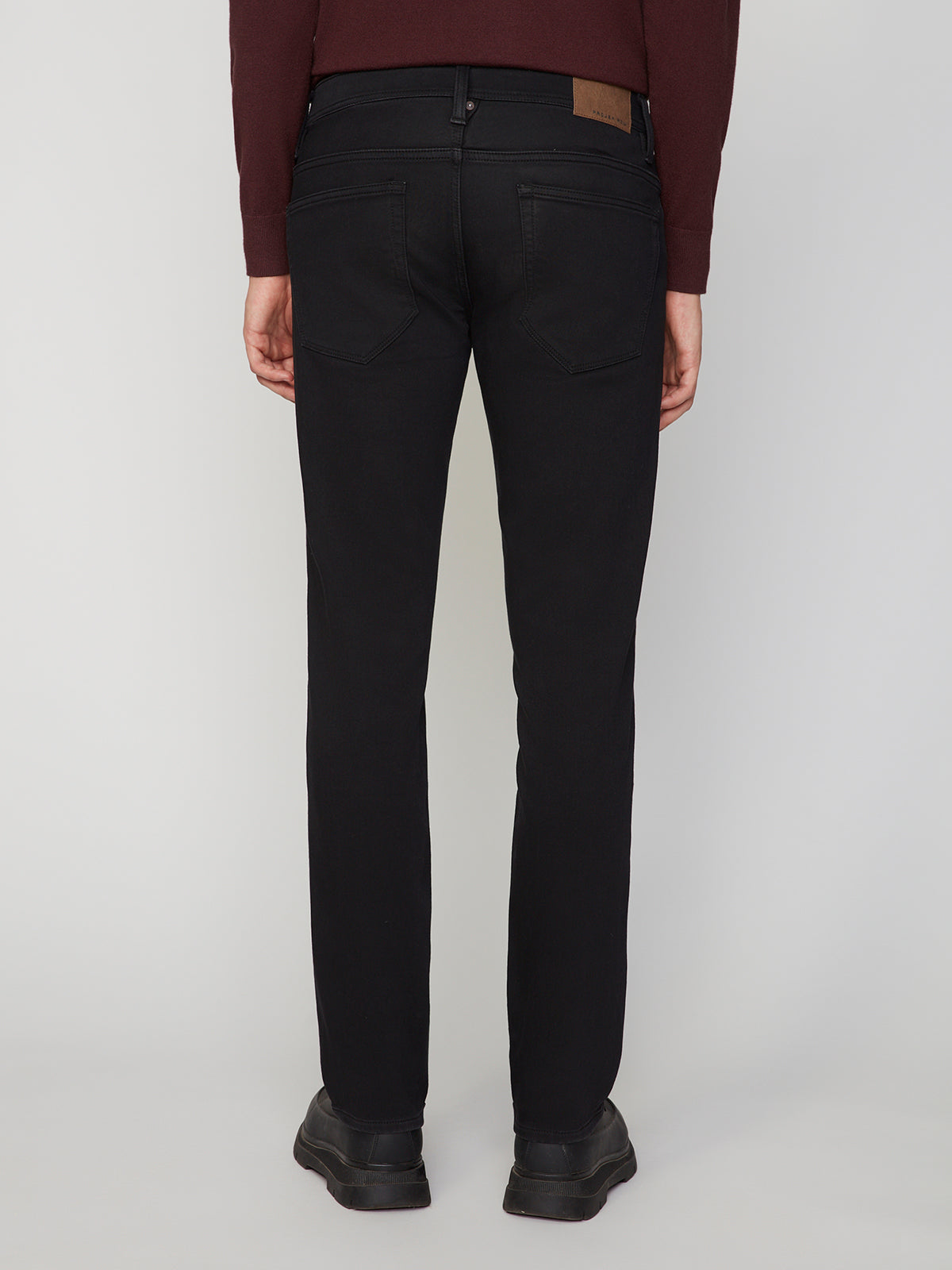 A person wearing PROJEK RAW MENS BARU STRAIGHT FIT COLORED DENIM JEAN in black, a burgundy long-sleeve shirt, and black shoes is standing facing away from the camera against a plain light background.
