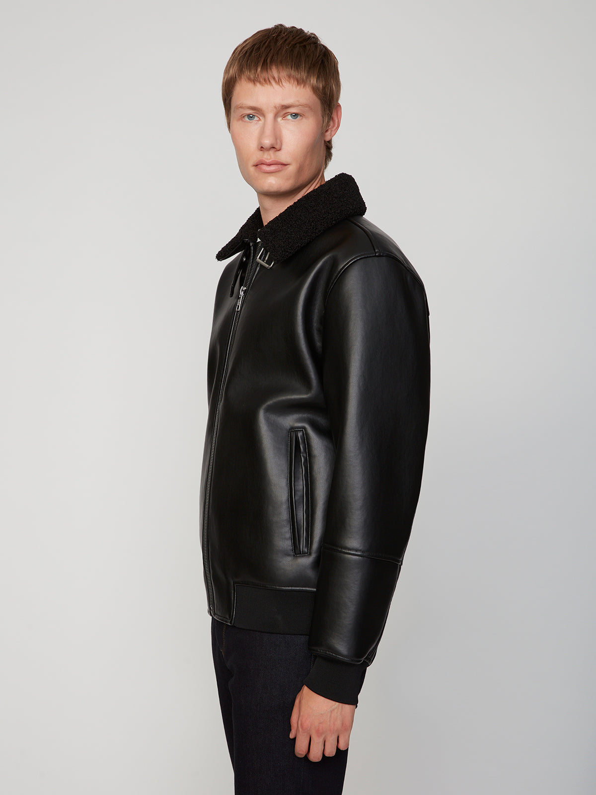 A young man with short light brown hair wears the PROJEK RAW MENS PU SHERPA LINED JACKET, standing against a plain light gray background and looking slightly toward the camera.