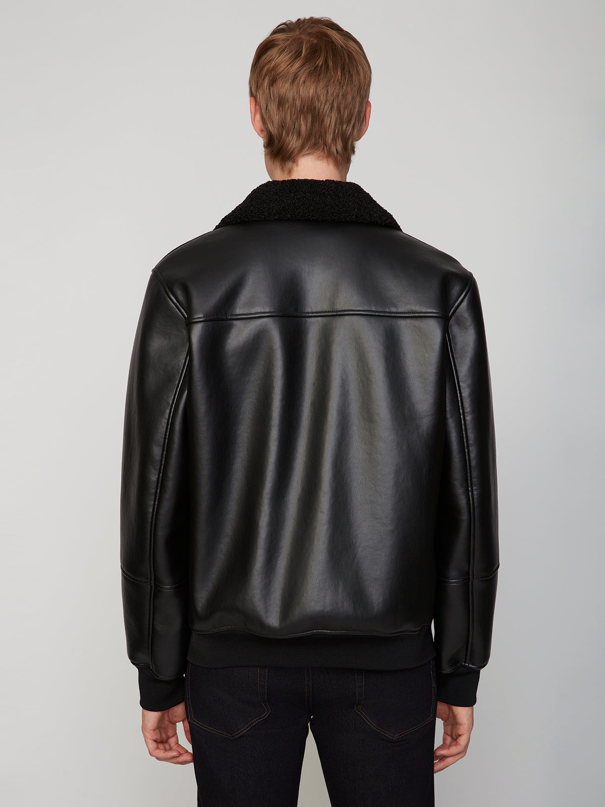 A person with light brown hair is shown from the back, wearing the PROJEK RAW MENS PU SHERPA LINED JACKET with a black sherpa collar and dark pants against a plain light background.