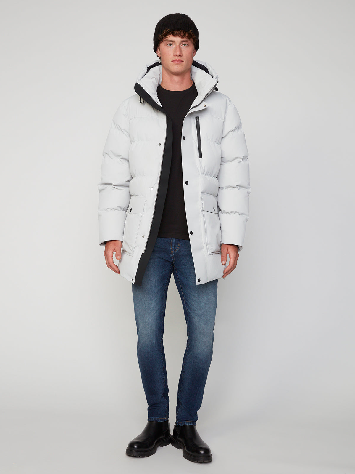 A person faces forward against a plain light background, wearing a black beanie, black shirt, blue jeans, black boots, and a white PROJEK RAW MENS TEXTURED RIPSTOP ECOFILL QUILTED PARKA WITH HOOD.
