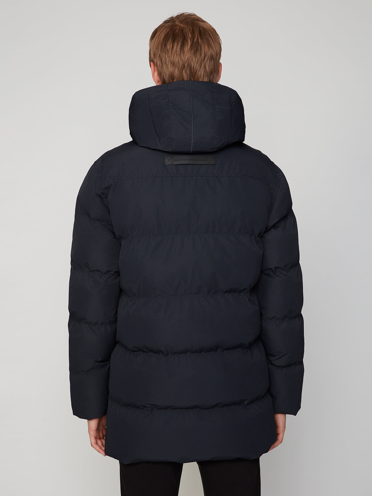 A person with light brown hair is shown from behind wearing the PROJEK RAW MENS TEXTURED RIPSTOP ECOFILL QUILTED PARKA WITH HOOD. The background is plain and light-colored.