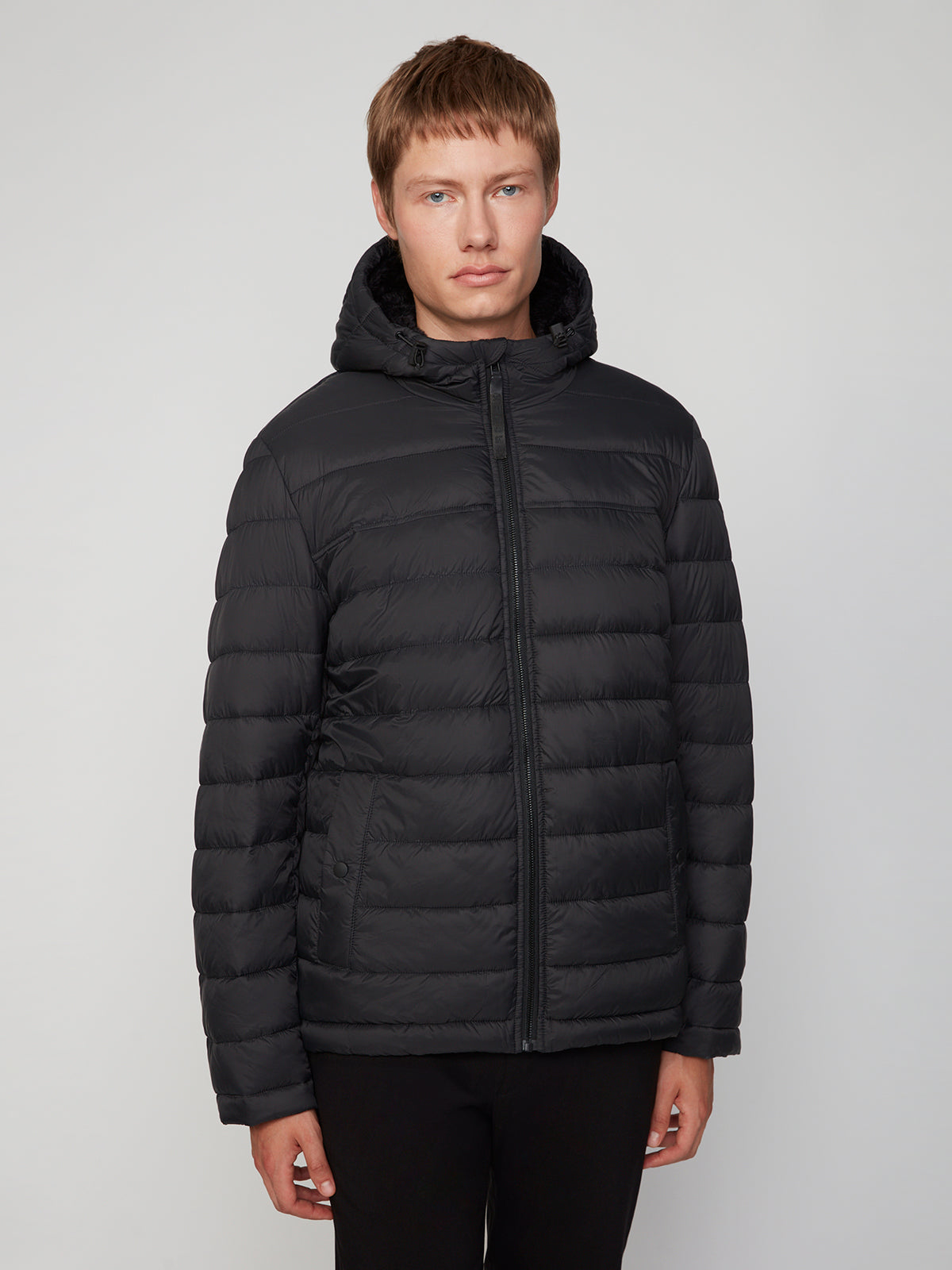 A man with short light brown hair wears the PROJEK RAW MENS HOODED FAUX FUR LINED PUFFER JACKET, standing against a plain light gray background and facing forward with a neutral expression.