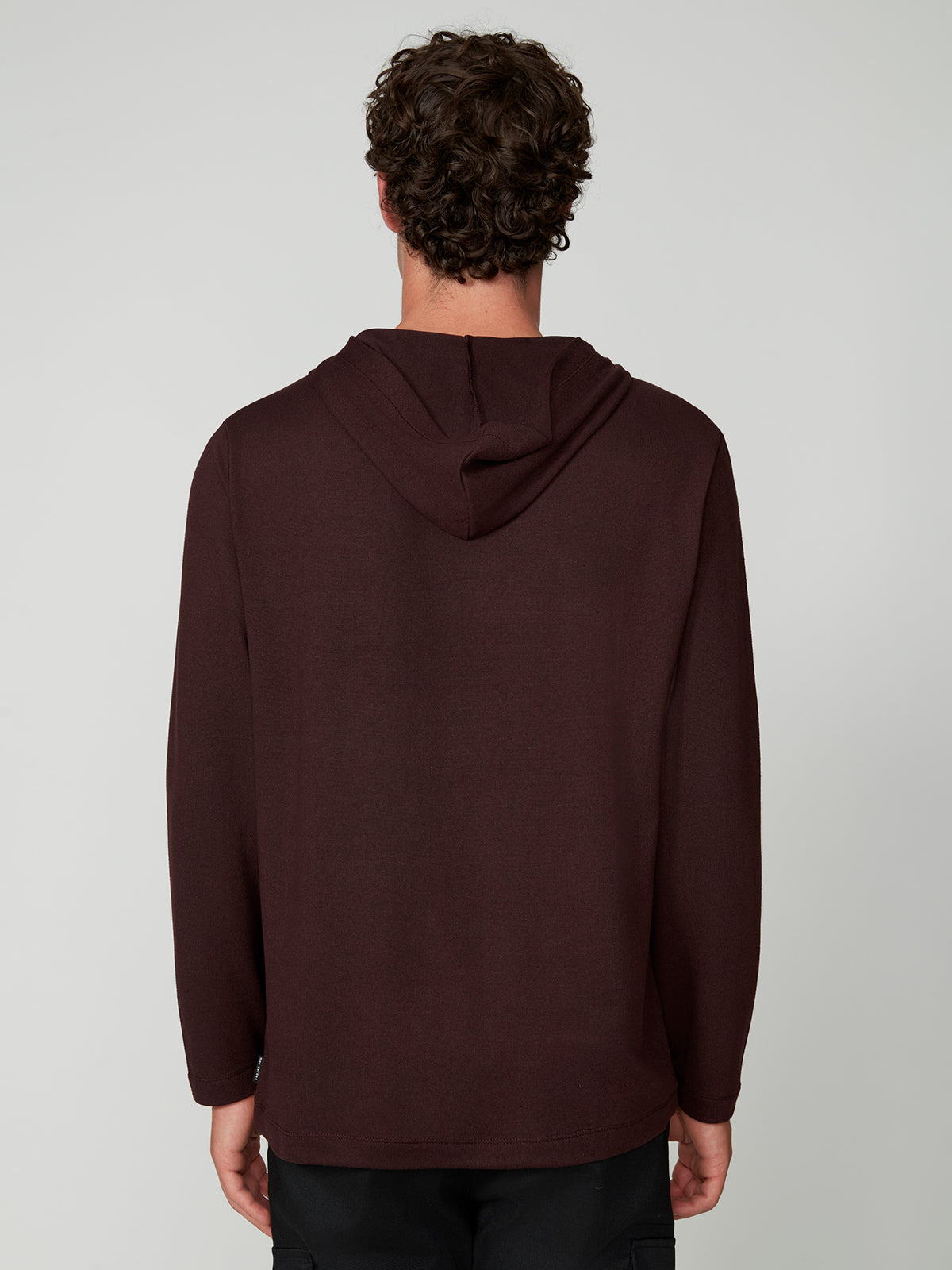 A person with curly brown hair is seen from behind, wearing the PROJEK RAW MENS HOODED LONG SLEEVE KNIT in dark maroon and black pants, standing against a plain light gray background.