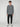 A young man with curly hair faces forward, wearing the PROJEK RAW MENS HOODED LONG SLEEVE KNIT in gray, paired with black jogger pants and white sneakers, embodying casual comfort against a plain light gray background.