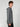A young man with curly brown hair stands sideways, facing left, wearing the PROJEK RAW MENS HOODED LONG SLEEVE KNIT in gray and black pants, showcasing casual comfort against a plain light gray background.