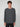 A young man with curly brown hair stands against a light gray background, wearing the PROJEK RAW MENS LONG SLEEVE CREW NECK KNIT in dark gray and black pants, looking casually at the camera with a neutral expression.