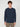 A young man with curly brown hair models the PROJEK RAW MENS LONG SLEEVE CREW NECK, a classic fit navy blue carbon peached jersey shirt with chest pocket, paired with khaki pants against a simple light gray background.