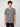 A young man with short curly brown hair wears a PROJEK RAW MENS SHORT SLEEVE CREW NECK GRID JERSEY OVERSIZE TSHIRT and black pants, standing against a light gray background and looking at the camera with a neutral expression.