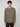 A young man with curly brown hair wears the PROJEK RAW MENS LONG SLEEVE CREW NECK in olive green stretch cotton jersey and black pants, standing against a plain light gray background, facing forward with a neutral expression.