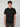 A young man with curly brown hair stands facing forward against a light gray background, showcasing the PROJEK RAW MENS SHORT SLEEVE SCUBA JERSEY RELAXED FIT TSHIRT in black and dark pants for a modern casual look.