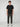 A young man with curly brown hair faces forward, wearing the PROJEK RAW MENS SHORT SLEEVE SCUBA JERSEY RELAXED FIT TSHIRT in black, paired with dark olive cargo pants and white sneakers against a plain light gray background—ideal for casual wear.