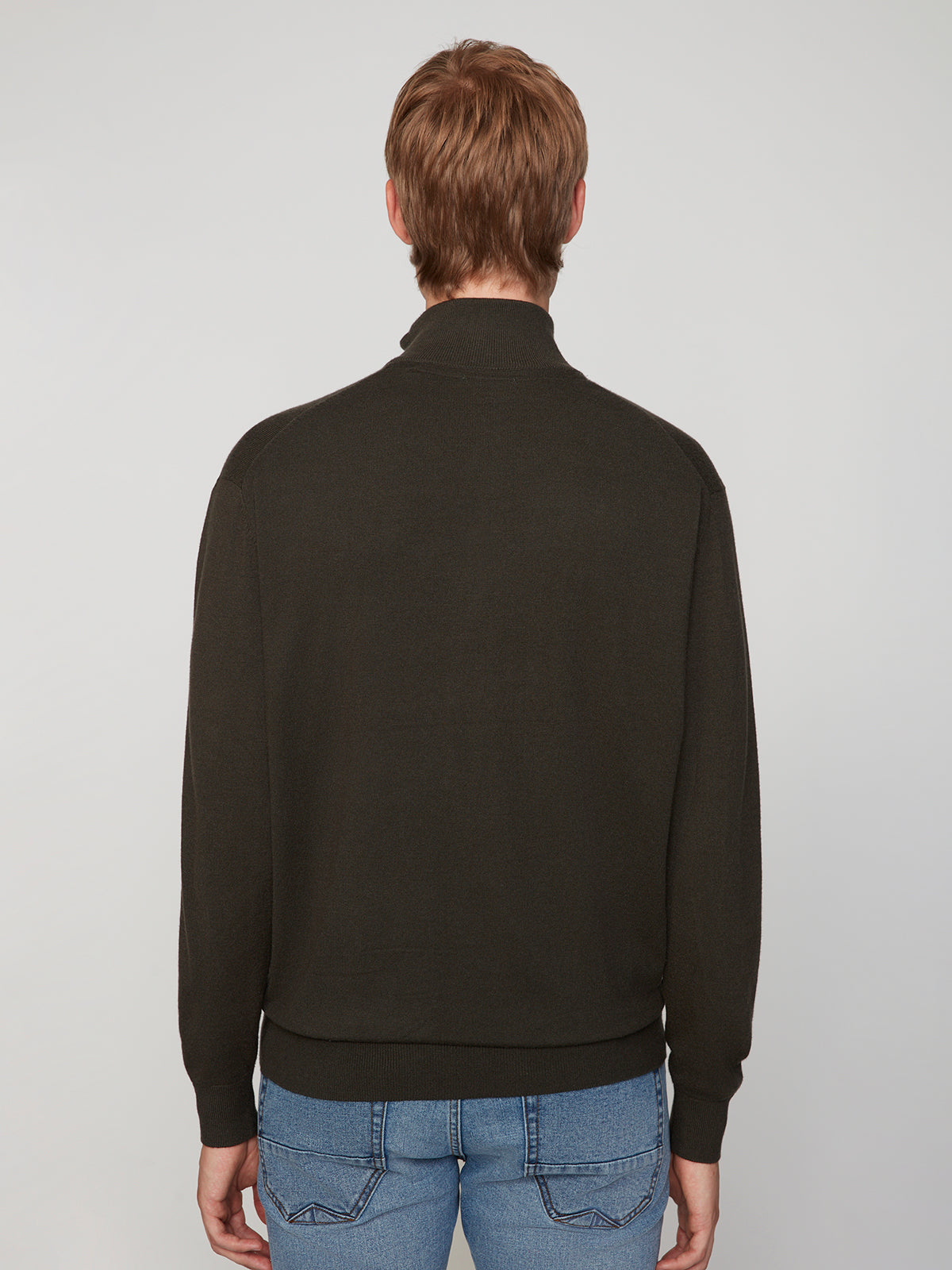 A person with short, light brown hair is shown from behind, wearing a dark PROJEK RAW MENS 1/4-ZIP CASHMERE TOUCH SWEATER and light blue jeans against a plain, light-colored background.