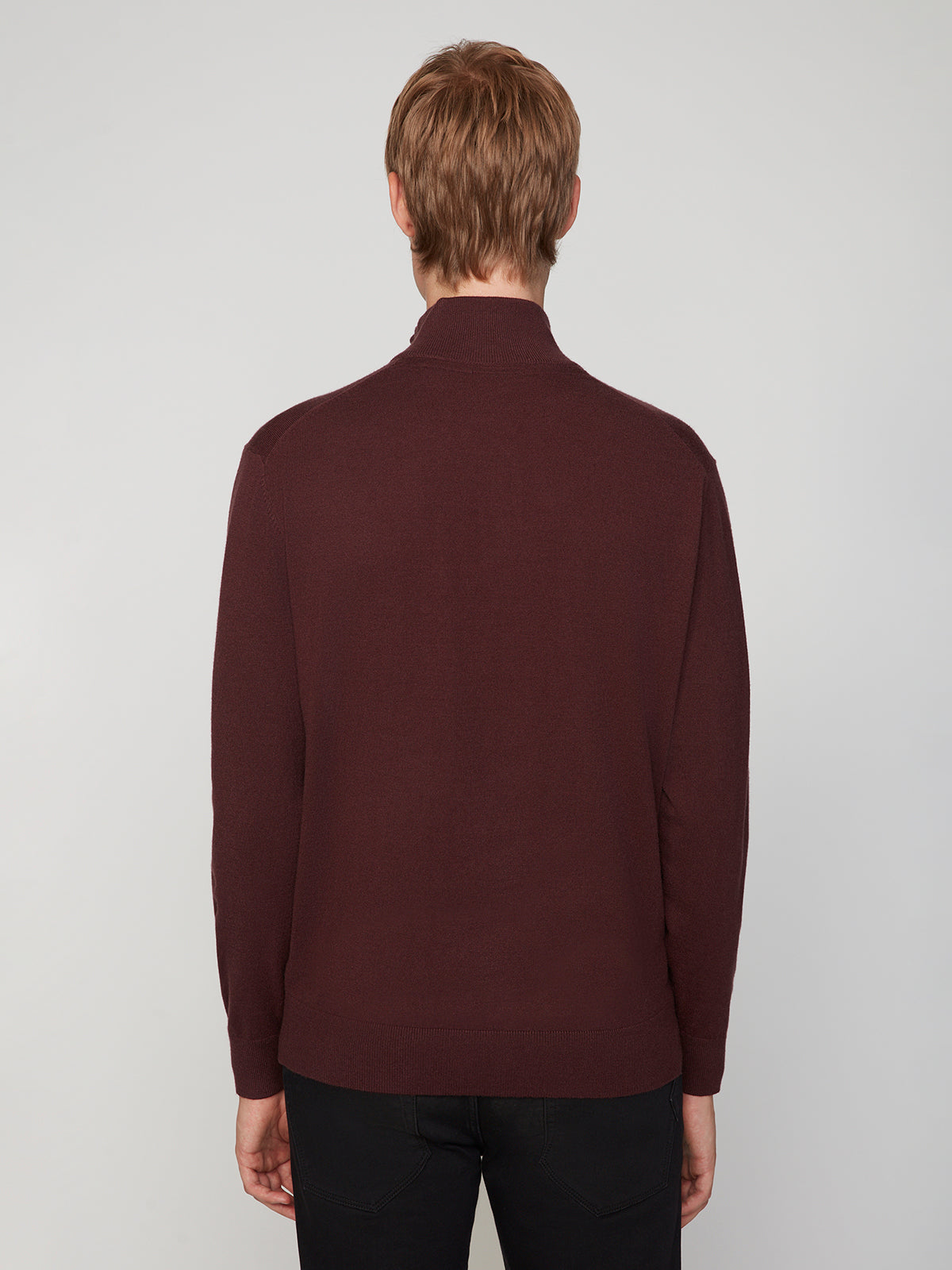 A person with short light brown hair faces away from the camera, wearing a PROJEK RAW MENS 1/4-ZIP CASHMERE TOUCH SWEATER in dark maroon and black pants, set against a plain light gray background.
