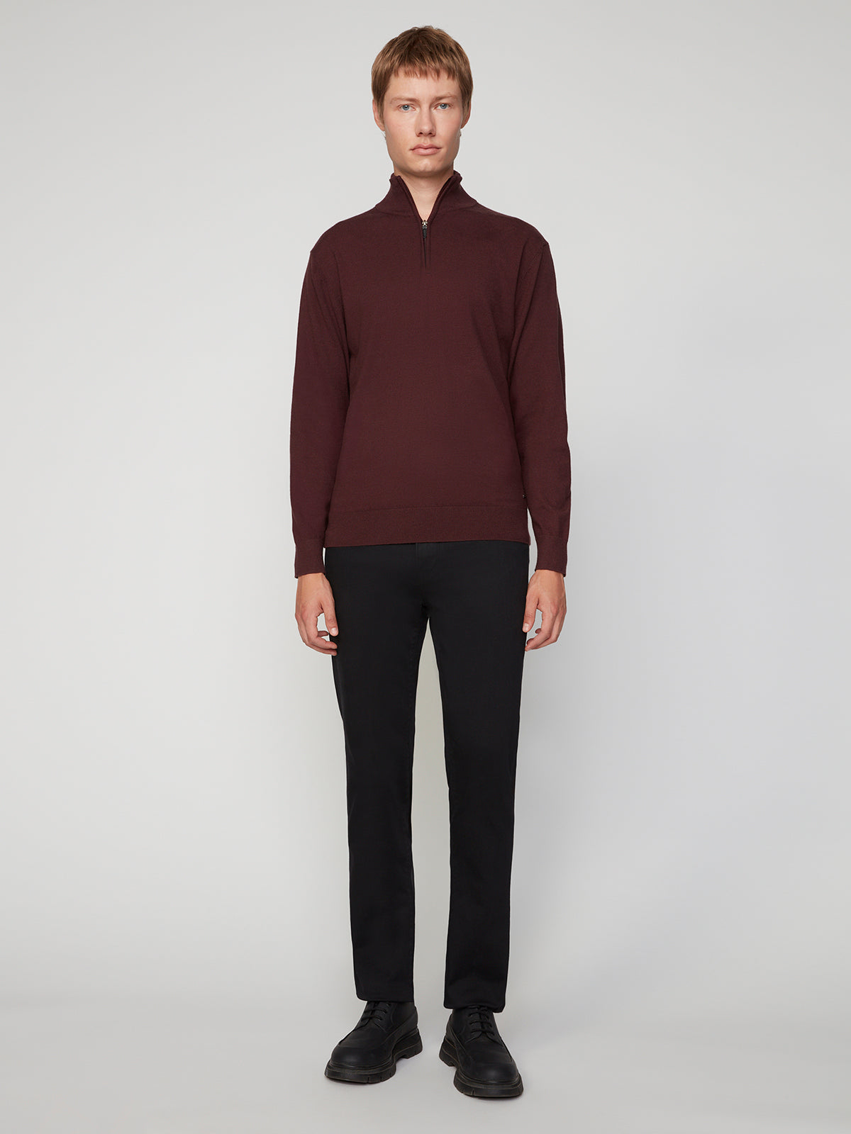 A person stands facing forward against a plain light background, wearing a dark red PROJEK RAW MENS 1/4-ZIP CASHMERE TOUCH SWEATER, black pants, and black shoes.