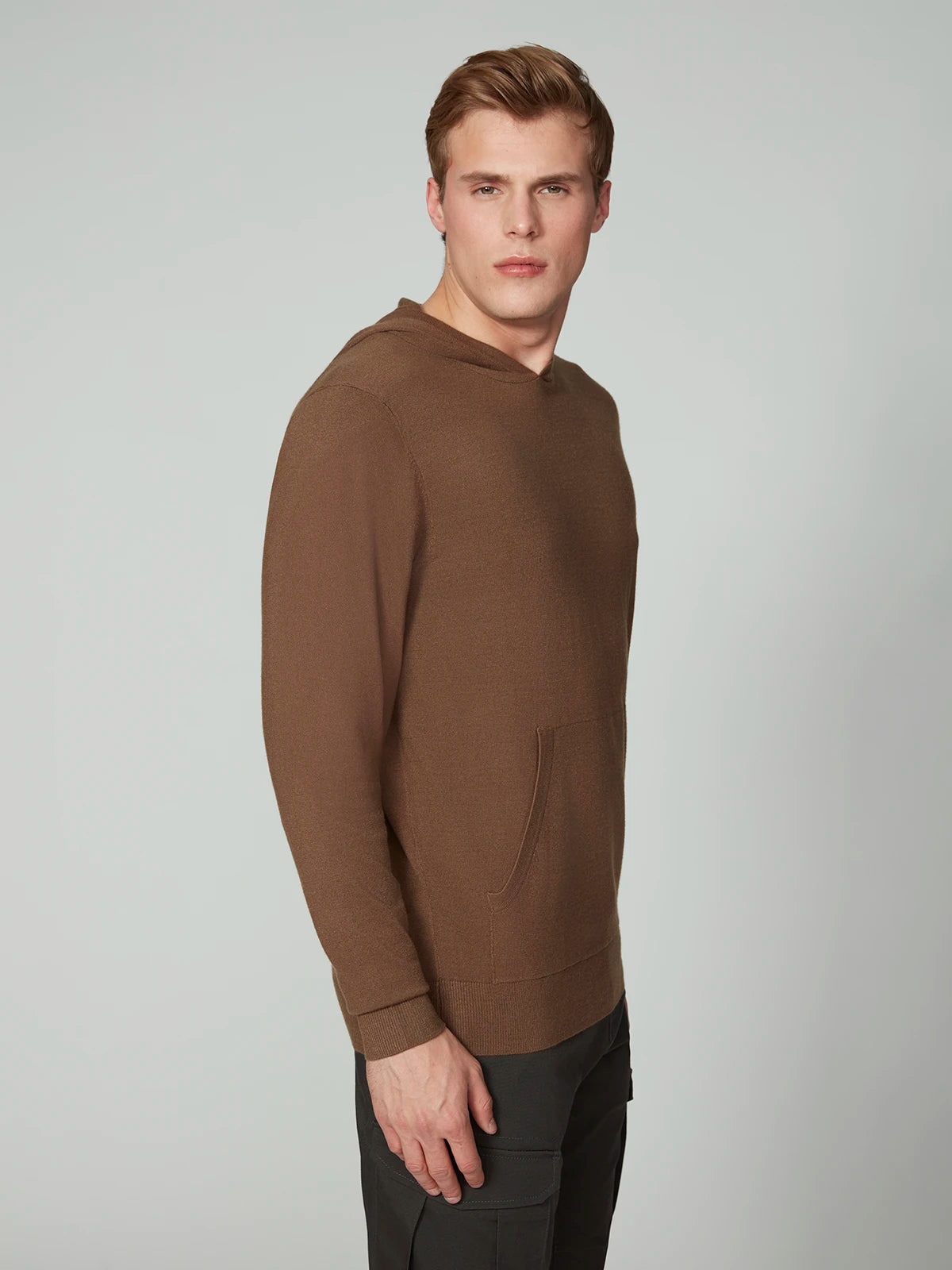 A young man with short light brown hair wears the PROJEK RAW MENS CASHMERE TOUCH HOODIE SWEATER and black pants, standing against a plain light gray background and looking slightly to the side.