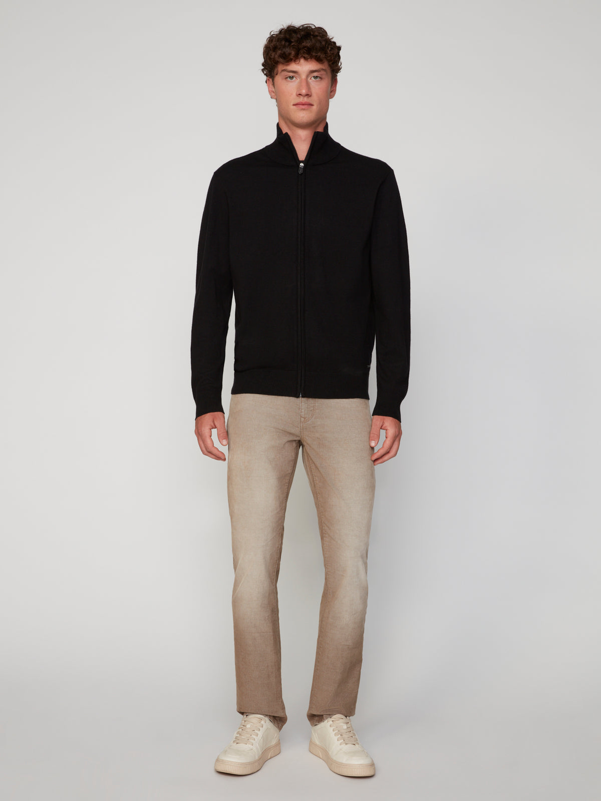 A man faces forward wearing a PROJEK RAW MENS ZIP-UP CASHMERE TOUCH SWEATER, light beige pants, and white sneakers against a plain light background.