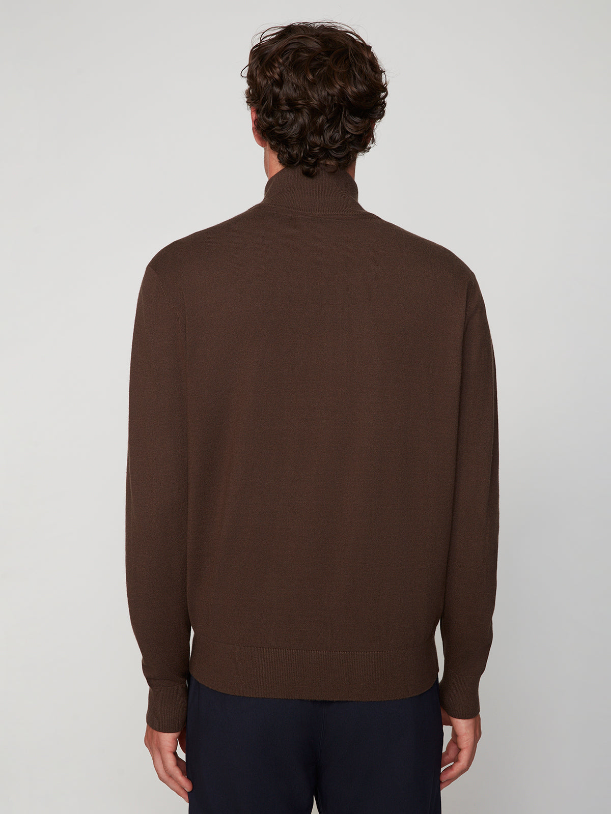 A person with short, curly brown hair is shown from the back, wearing a PROJEK RAW MENS ZIP-UP CASHMERE TOUCH SWEATER and dark pants, standing against a plain light background.
