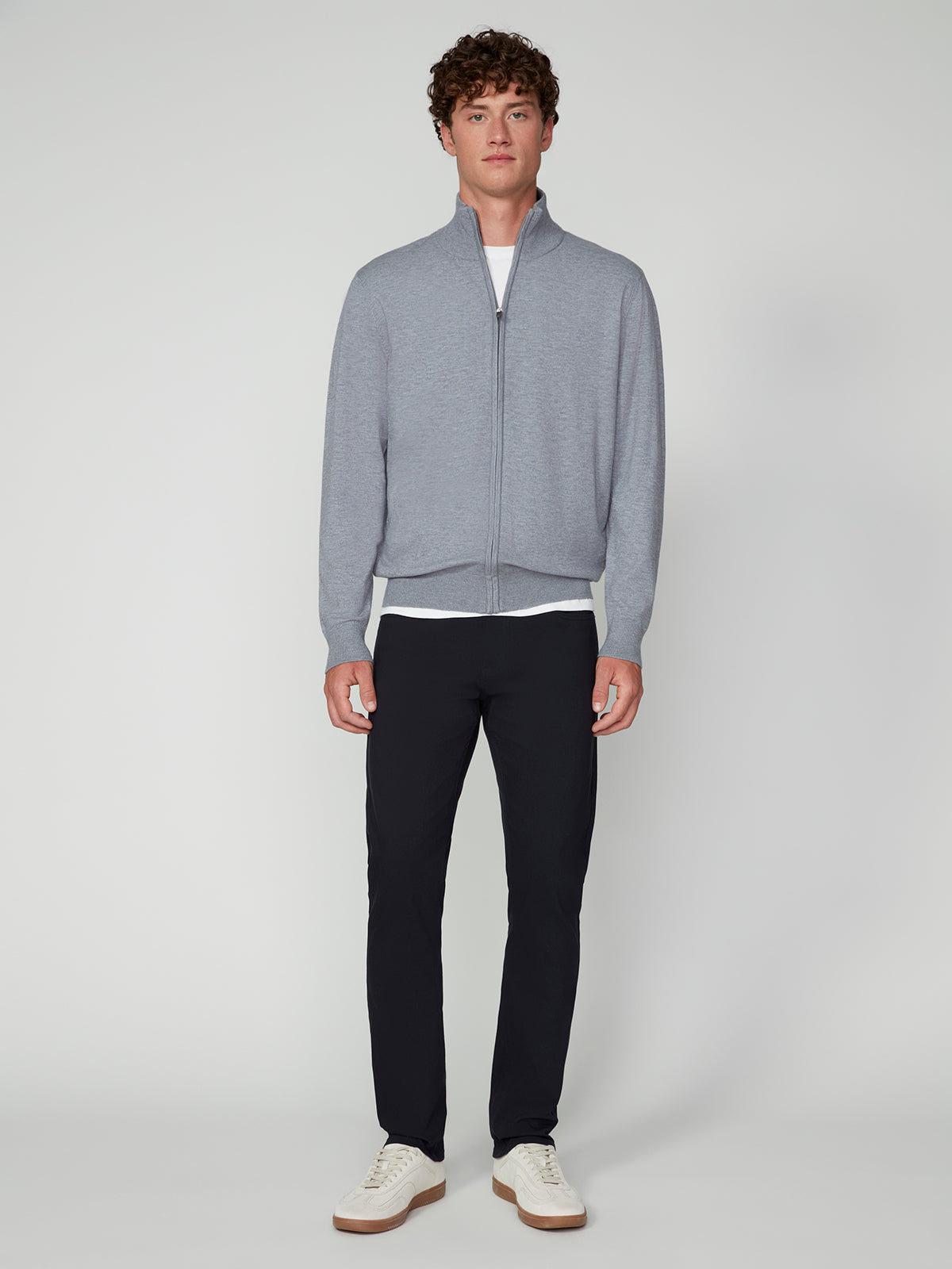 A person stands facing forward, wearing the PROJEK RAW MENS ZIP-UP CASHMERE TOUCH SWEATER in light gray over a white shirt, paired with dark slim pants and white sneakers, set against a plain light gray background.