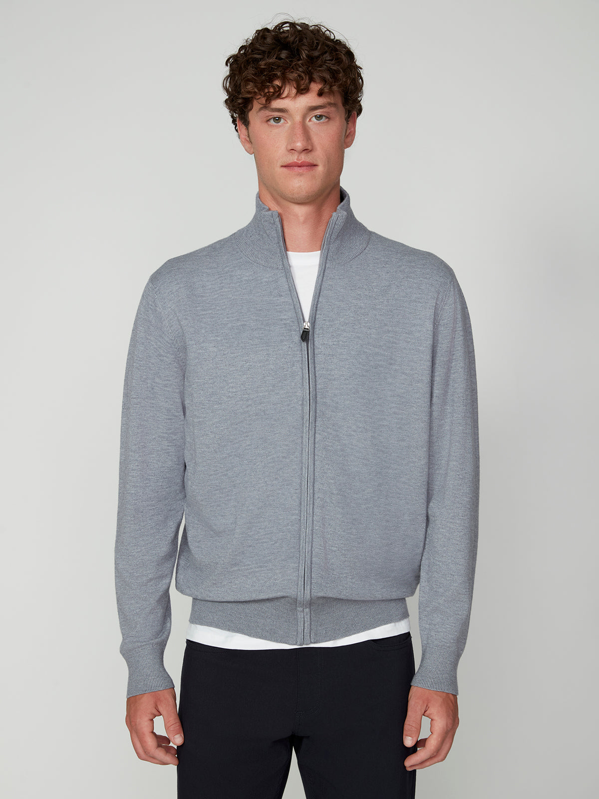A young man with curly brown hair wears a light gray PROJEK RAW MENS ZIP-UP CASHMERE TOUCH SWEATER over a white t-shirt, standing against a plain, light background and looking directly at the camera with a neutral expression.