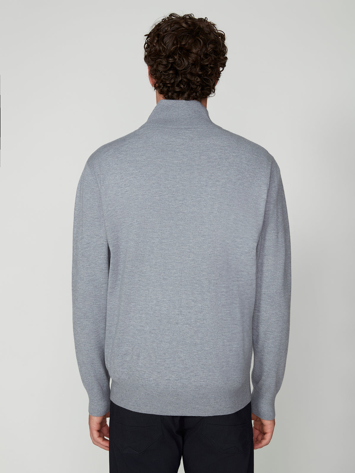 A man with curly hair stands with his back to the camera, wearing a light gray PROJEK RAW MENS ZIP-UP CASHMERE TOUCH SWEATER and dark pants against a plain white background.
