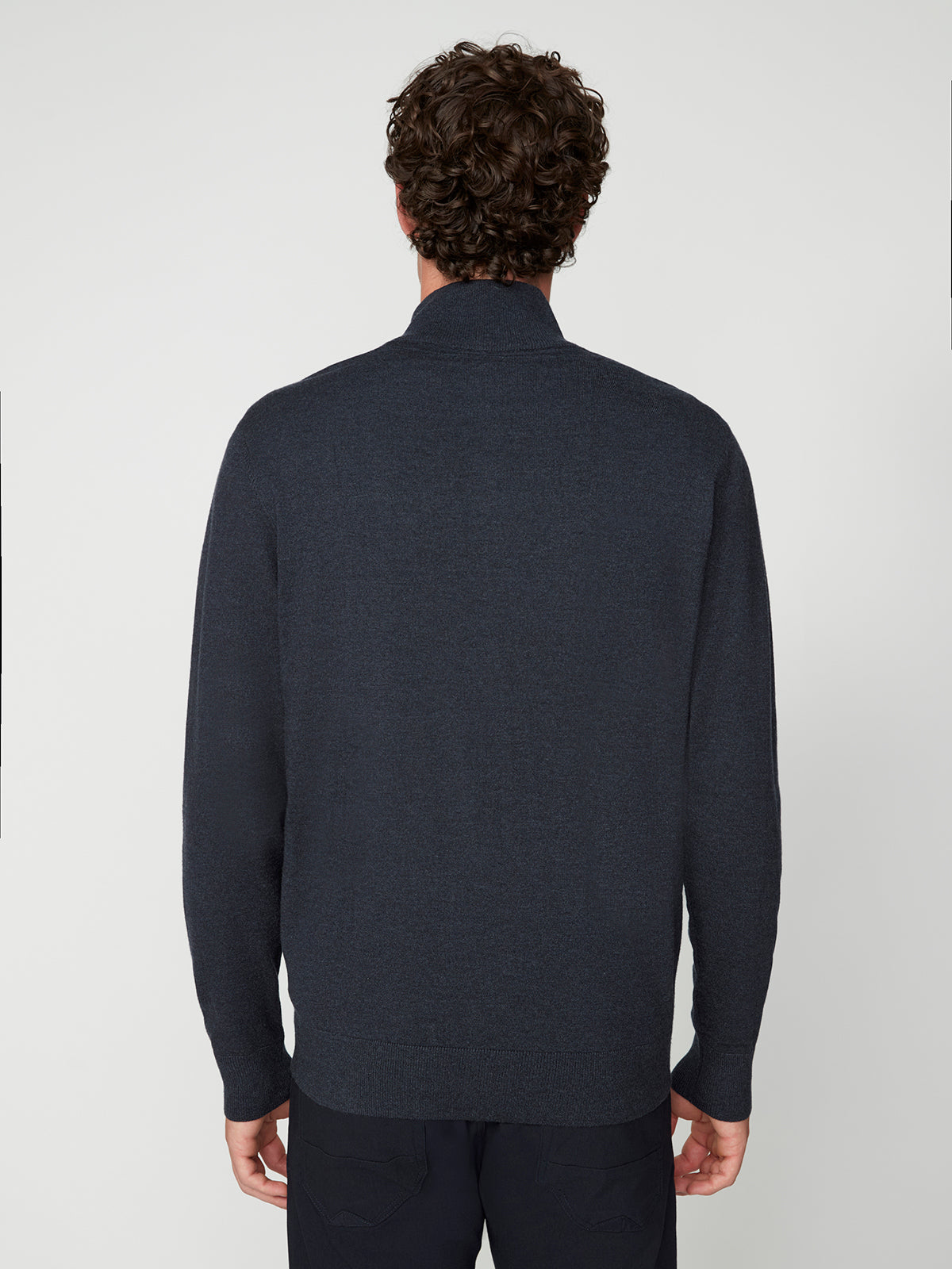 A man with curly dark hair, seen from behind, wears a dark navy PROJEK RAW MENS ZIP-UP CASHMERE TOUCH SWEATER and dark pants against a plain light background.