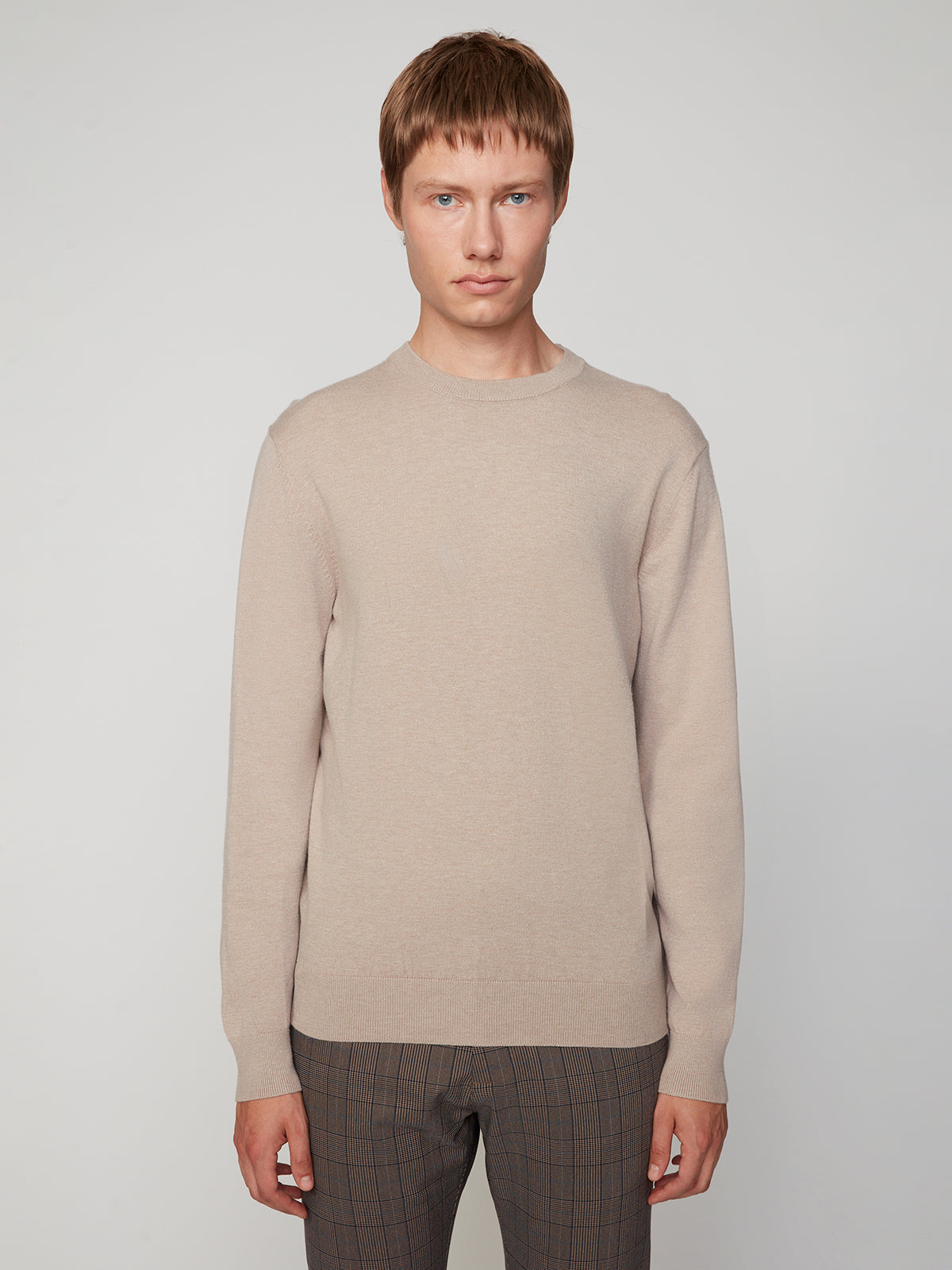 A man with short light brown hair wears a PROJEK RAW MENS CREW NECK CASHMERE TOUCH SWEATER in beige and brown plaid pants, standing against a plain light gray background, facing forward with a neutral expression.