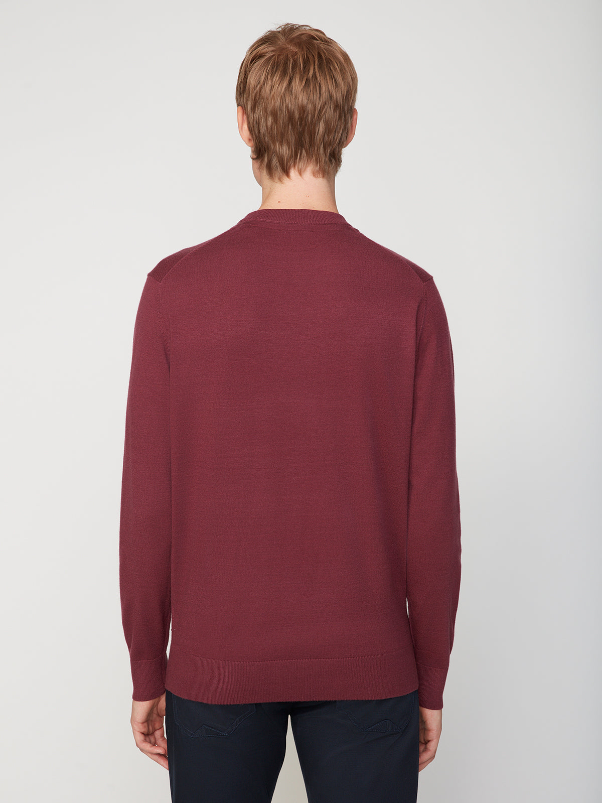 A person with short, light brown hair is seen from the back, wearing a PROJEK RAW MENS CREW NECK CASHMERE TOUCH SWEATER in dark red and dark pants against a plain, light gray background.