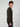 A young man with curly brown hair stands sideways, looking at the camera. He wears a PROJEK RAW MENS CREW NECK CASHMERE TOUCH SWEATER in dark green with dark pants, set against a plain light gray background.