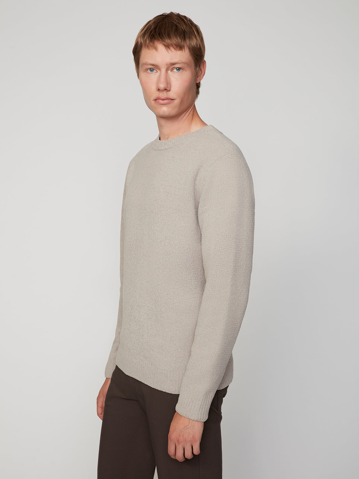 A person with short, light brown hair wears the PROJEK RAW MENS CREW NECK CHENILLE SWEATER in light beige with dark pants, standing against a plain light gray background and facing slightly to the side with a neutral expression.