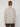 A person with short light brown hair stands facing away from the camera, wearing the PROJEK RAW MENS CREW NECK CHENILLE SWEATER in light beige and dark pants against a plain white background.