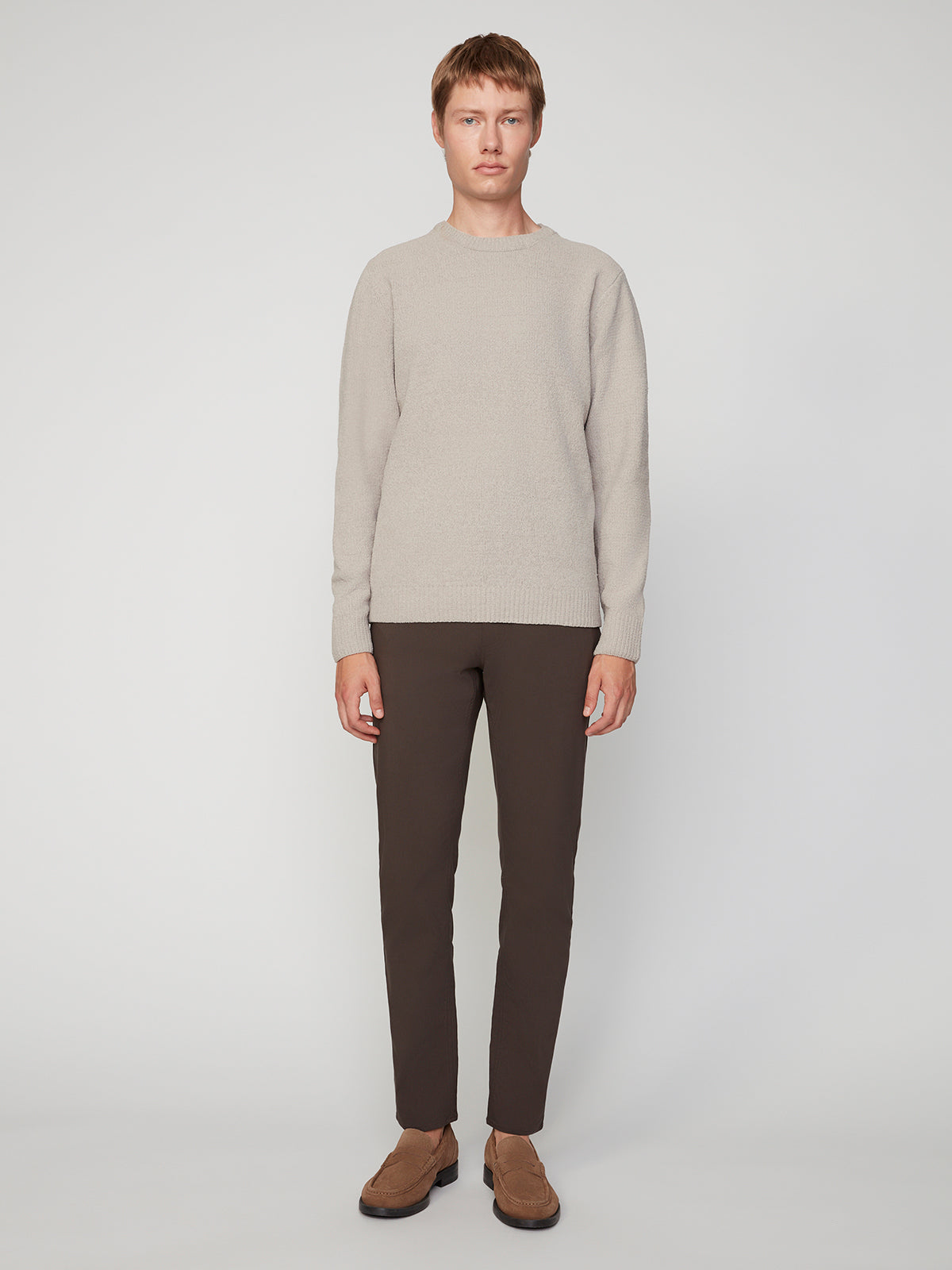 A person stands facing forward against a plain, light background, wearing the PROJEK RAW MENS CREW NECK CHENILLE SWEATER in light beige, paired with dark brown pants and brown shoes.