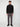 A young man with short curly hair and a neutral expression stands against a plain background, wearing the PROJEK RAW MENS CHENILLE MOCK NECK SWEATER in black, paired with gray slim-fit pants and black shoes.