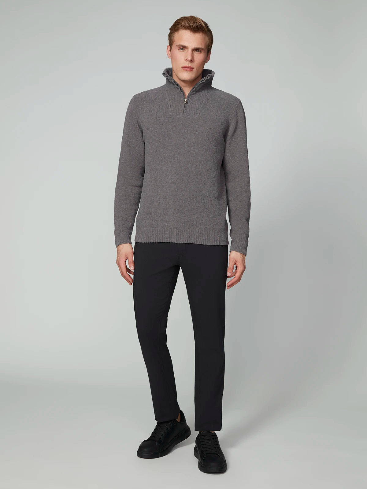 A man stands against a plain light background wearing the PROJEK RAW MENS CHENILLE MOCK NECK SWEATER in gray, paired with black pants and black sneakers. He faces forward with a neutral expression and relaxed posture.