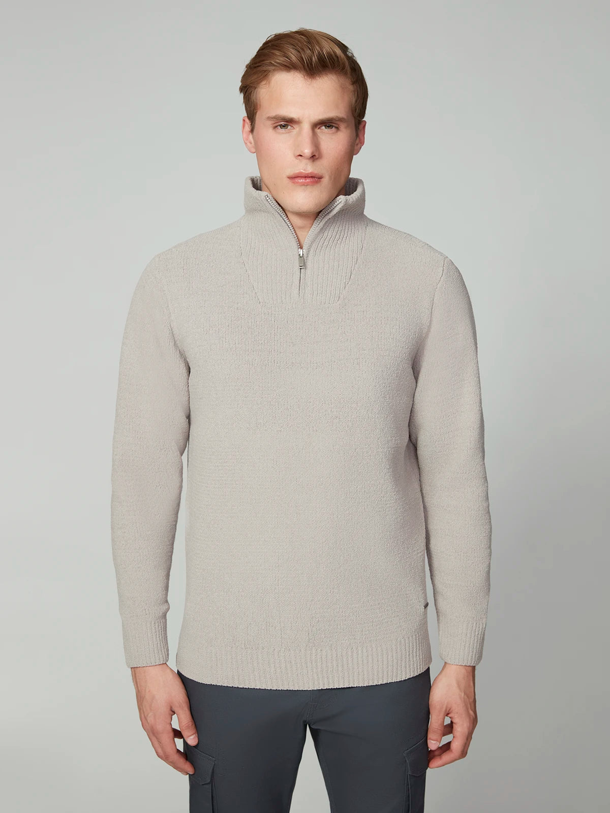 A man with short light brown hair wears the PROJEK RAW MENS CHENILLE MOCK NECK SWEATER in light gray and dark pants, standing against a plain light gray background and looking directly at the camera with a neutral expression.