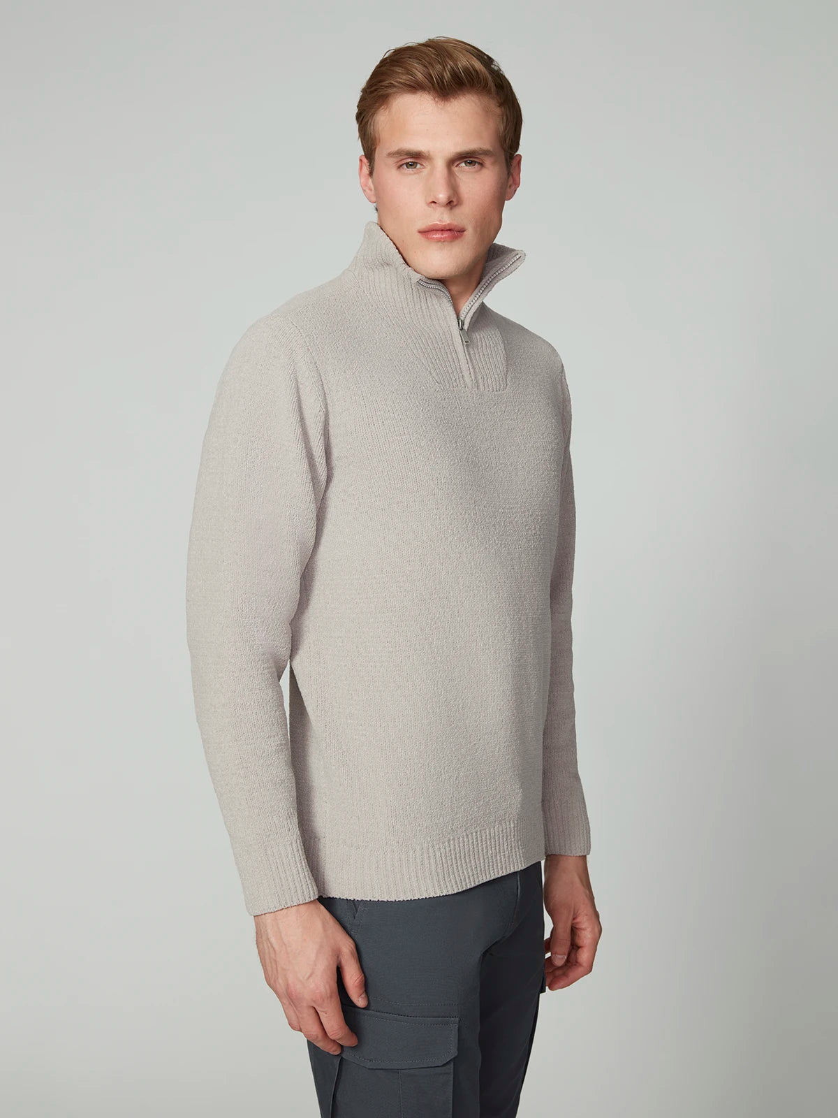 A young man with short light brown hair wears the PROJEK RAW MENS CHENILLE MOCK NECK SWEATER in light gray and dark gray pants. He stands against a plain light background, looking slightly to the side.