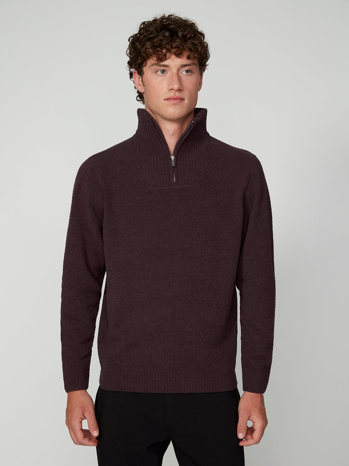 A young man with curly brown hair wears a PROJEK RAW MENS CHENILLE MOCK NECK SWEATER in dark maroon and black pants, standing against a plain light gray background, looking straight ahead with a neutral expression.