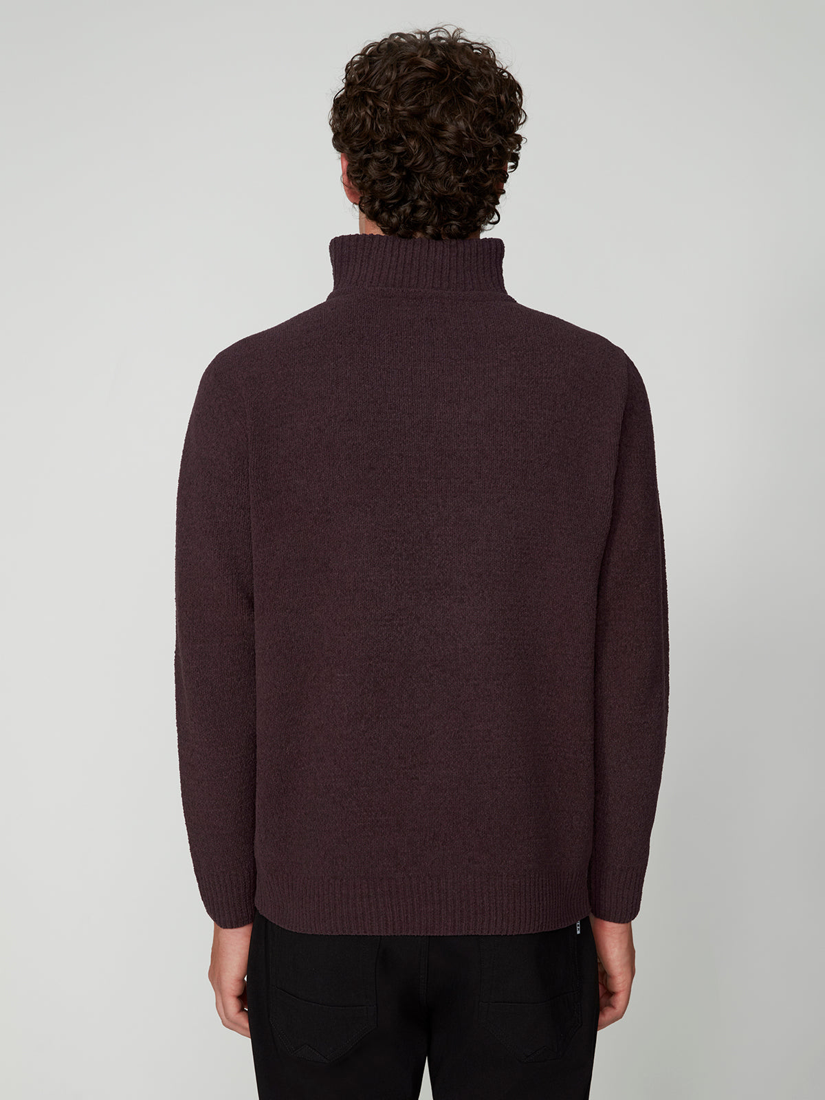 A person with short curly hair is seen from behind, wearing a dark maroon PROJEK RAW MENS CHENILLE MOCK NECK SWEATER and black pants, standing against a plain light gray background.