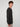 A young man with curly brown hair wears a PROJEK RAW MENS SHAKER RIB KNIT SWEATER in a dark shade and light pants, standing sideways and looking toward the camera against a plain light background.