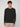 A young man with curly brown hair wears the PROJEK RAW MENS SHAKER RIB KNIT SWEATER in black and light beige pants, standing against a plain light gray background, facing forward with a neutral expression.