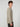 A young man with curly brown hair wears the PROJEK RAW MENS SHAKER RIB KNIT SWEATER in beige and dark pants, standing in profile against a plain light gray background.