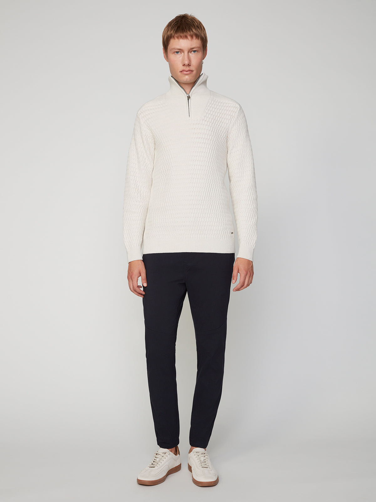 A person stands against a plain background wearing the PROJEK RAW MENS 1/4 ZIP JACQUARD KNIT MOCK NECK SWEATER, dark pants, and white sneakers. They face forward with a neutral expression and arms at their sides.
