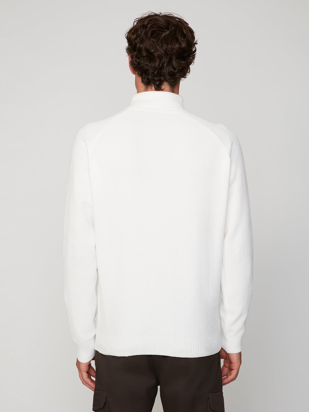 A person with short, curly brown hair is seen from behind wearing a PROJEK RAW MENS CHENILLE MOCK NECK SWEATER in white and dark pants against a plain light gray background.