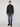 A person with short hair faces forward, wearing PROJEK RAW MENS FULL ZIPPED KNIT SWEATER BONDED POLAR FLEECE, blue jeans, and black shoes against a plain light gray background.