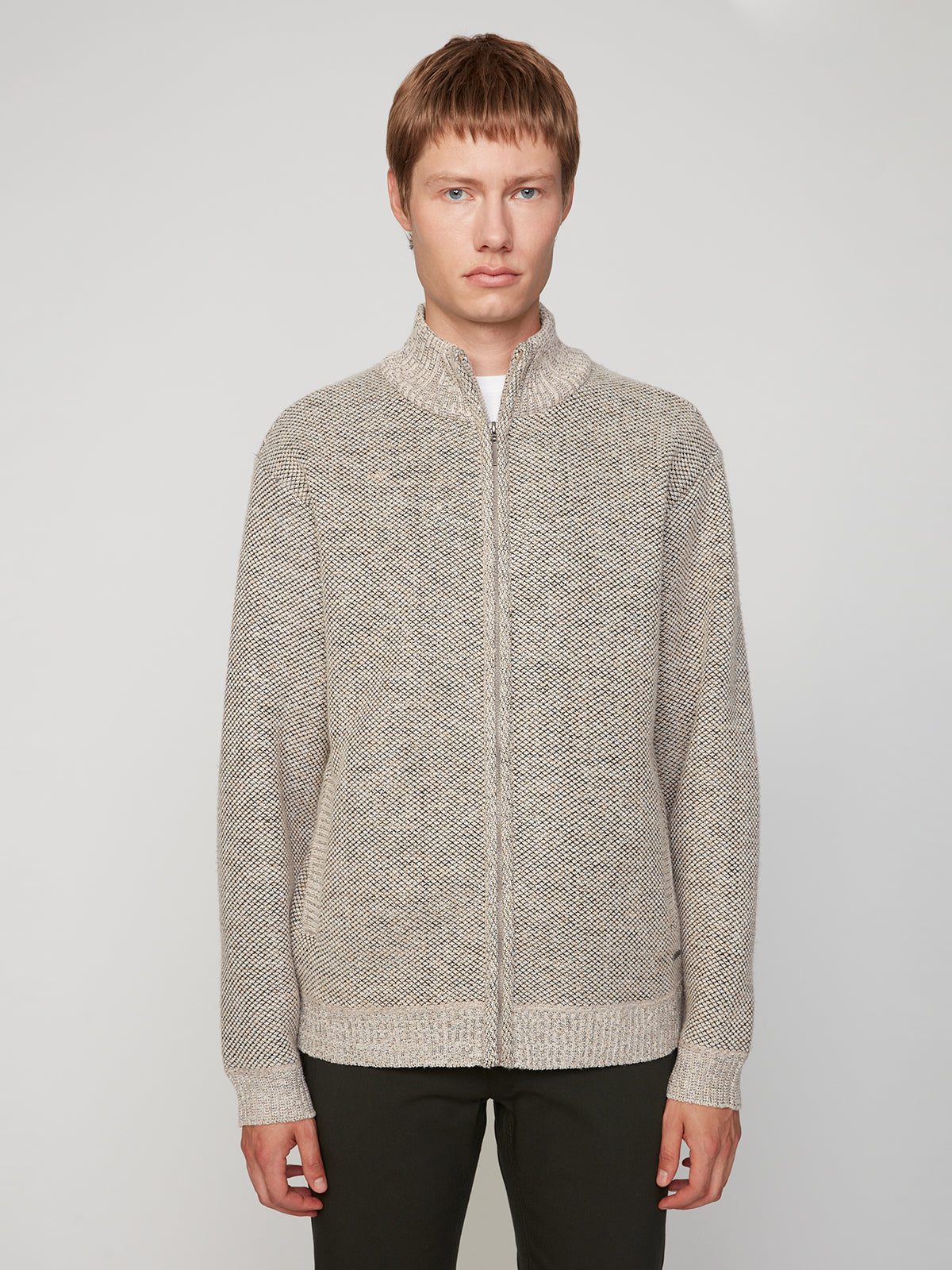 A person with short light brown hair wears the PROJEK RAW MENS FULL ZIPPED KNIT SWEATER BONDED POLAR FLEECE in beige, featuring a subtle knit texture, and stands against a plain light gray background.