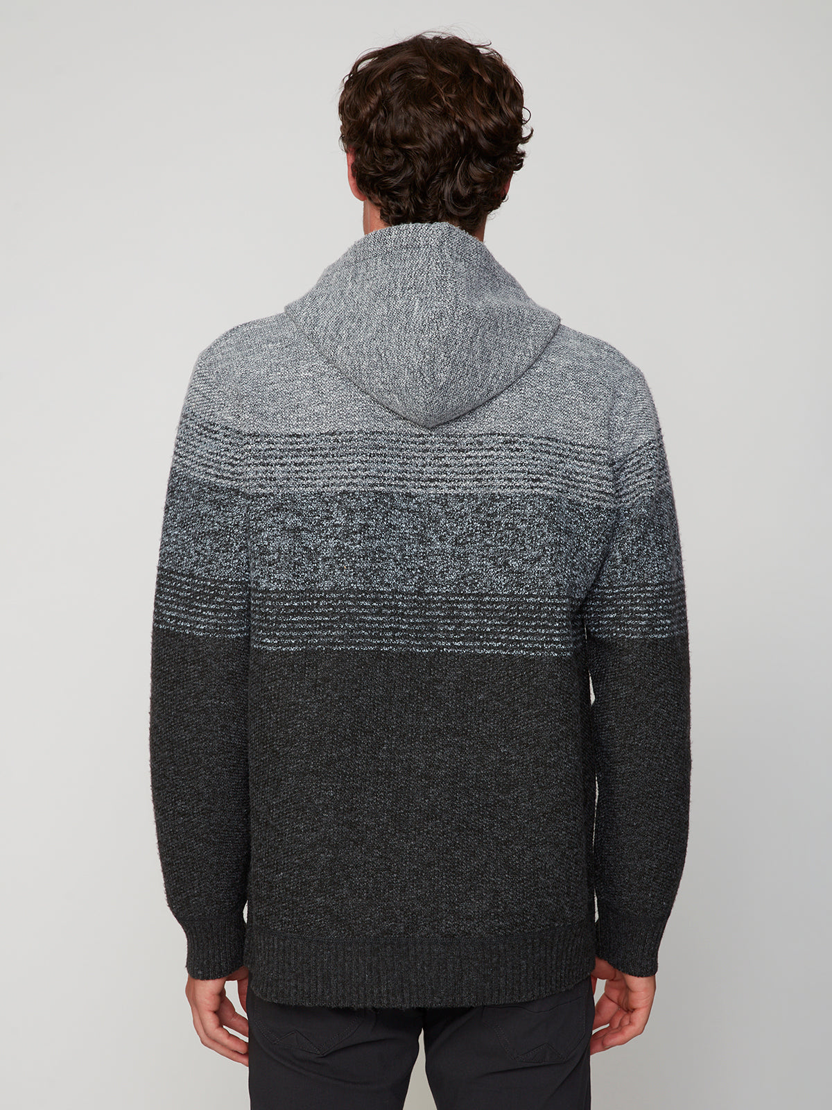 A man with curly brown hair faces away, wearing the PROJEK RAW MENS KNIT HOODED SWEATER BONDED WITH POLAR FLEECE, featuring gradient stripes and long sleeves, against a plain light background.