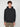 A young man with curly brown hair models the PROJEK RAW MENS LONG SLEEVE CARBON PEACHED FLEECE HOODIE in black and beige pants, standing against a light gray background with a neutral expression and relaxed hands by his sides.