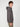 A young man with curly hair models the PROJEK RAW MENS LONG SLEEVE CARBON PEACHED FLEECE HOODIE in gray and khaki pants, standing sideways and looking toward the camera against a plain white background.
