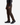 A person wearing the PROJEK RAW SOLID BUNGEE 5-POCKET PANTS in dark brown, paired with a dark plaid shirt and black sneakers, stands against a plain white background. Only the lower half of the body is visible.