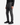 A person wearing PROJEK RAW SOLID BUNGEE CARGO PANT for men in dark gray with utility pockets, paired with a black button-up shirt and black sneakers, standing against a plain white background.